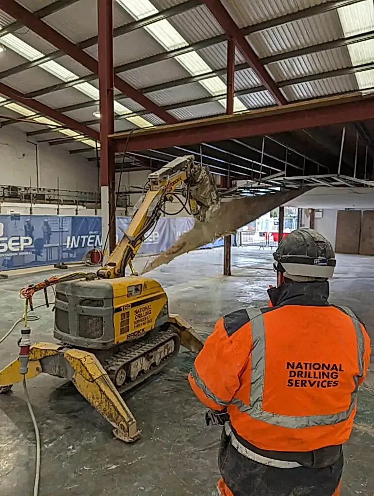 Robotic demolition machine operated by worker in safety gear, showcasing National Drilling Services' expertise in controlled demolition within industrial setting.