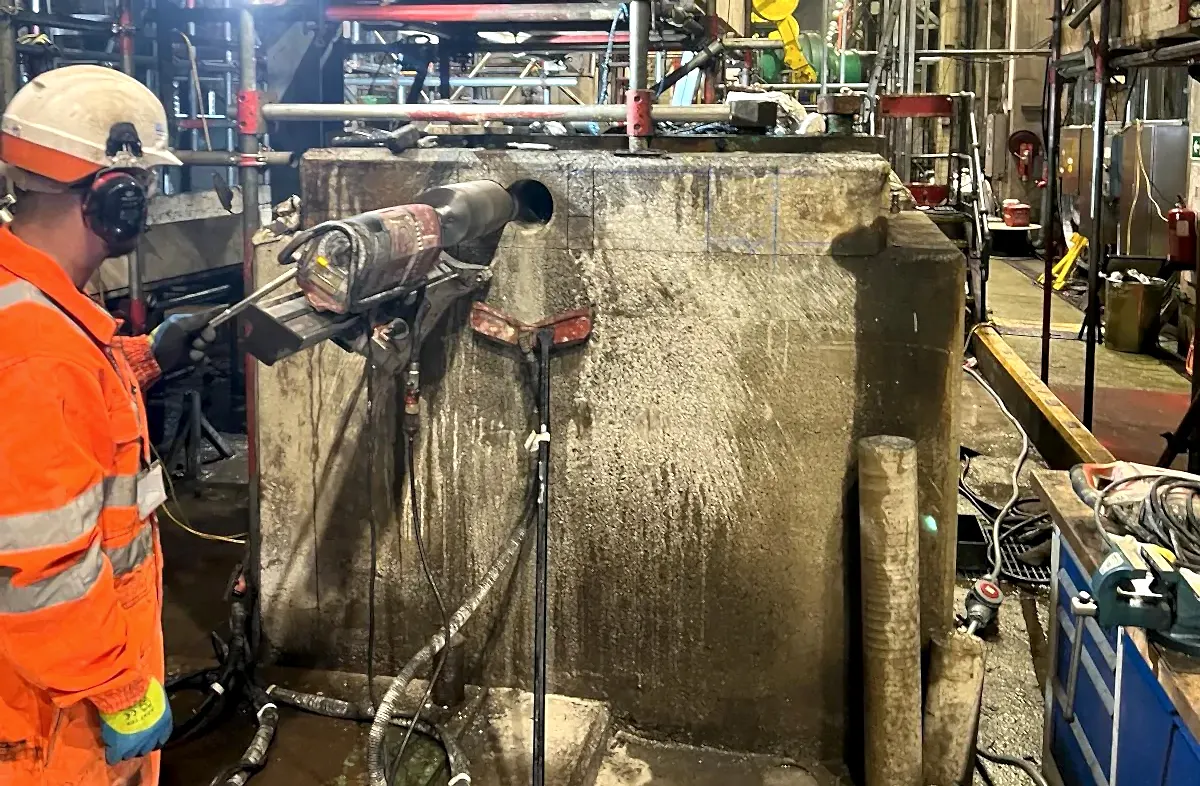 Worker operating diamond core drilling equipment on concrete surface in industrial setting, showcasing National Drilling Services' concrete core drilling capabilities.