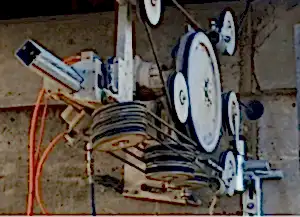 Diamond wire sawing machine mounted on a wall, featuring multiple pulleys and cutting wires, illustrating precision cutting capabilities for reinforced concrete by National Drilling Services.
