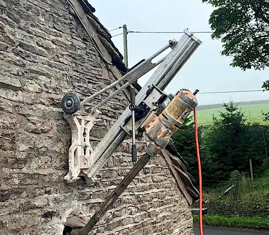 Concrete drilling equipment mounted on a stone wall, demonstrating domestic drilling services for extractor fans and ventilation systems by National Drilling Services.