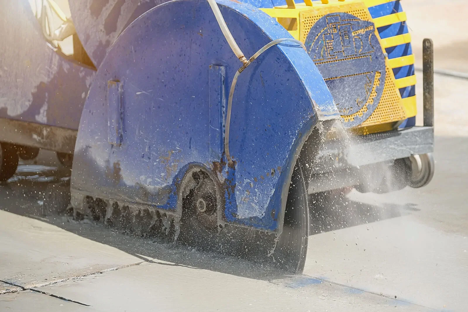 Blue expansion joint cutting saw in action, demonstrating precision cutting for construction projects, with water spray for dust control.
