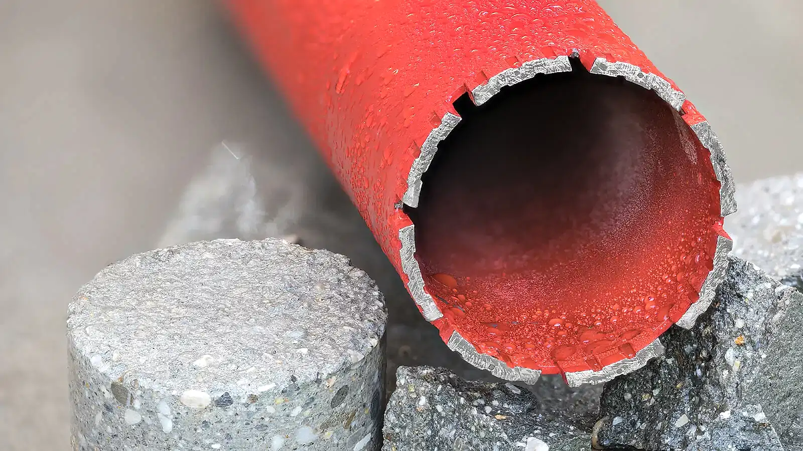 Red diamond wire saw blade with droplets of water, resting on a concrete surface, showcasing National Drilling Services' concrete cutting technology.