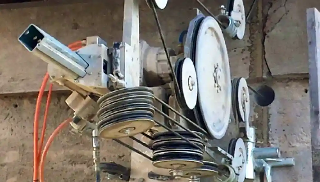 Wire sawing equipment with pulleys and drive mechanisms, used for efficient cutting in construction and demolition projects, featuring orange cables and mounted on a concrete wall.