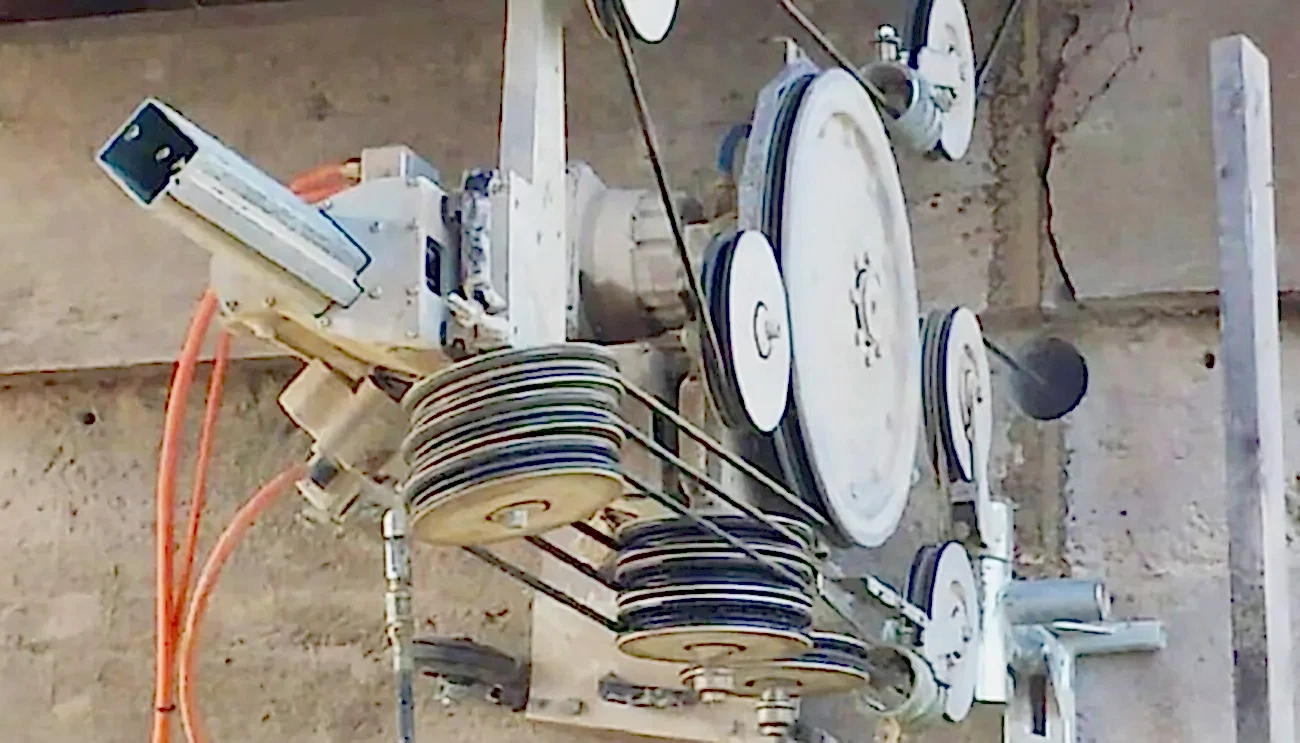 Wire sawing equipment mounted on a concrete wall, showcasing pulleys and a motor, used for precise cutting in drilling and demolition services.