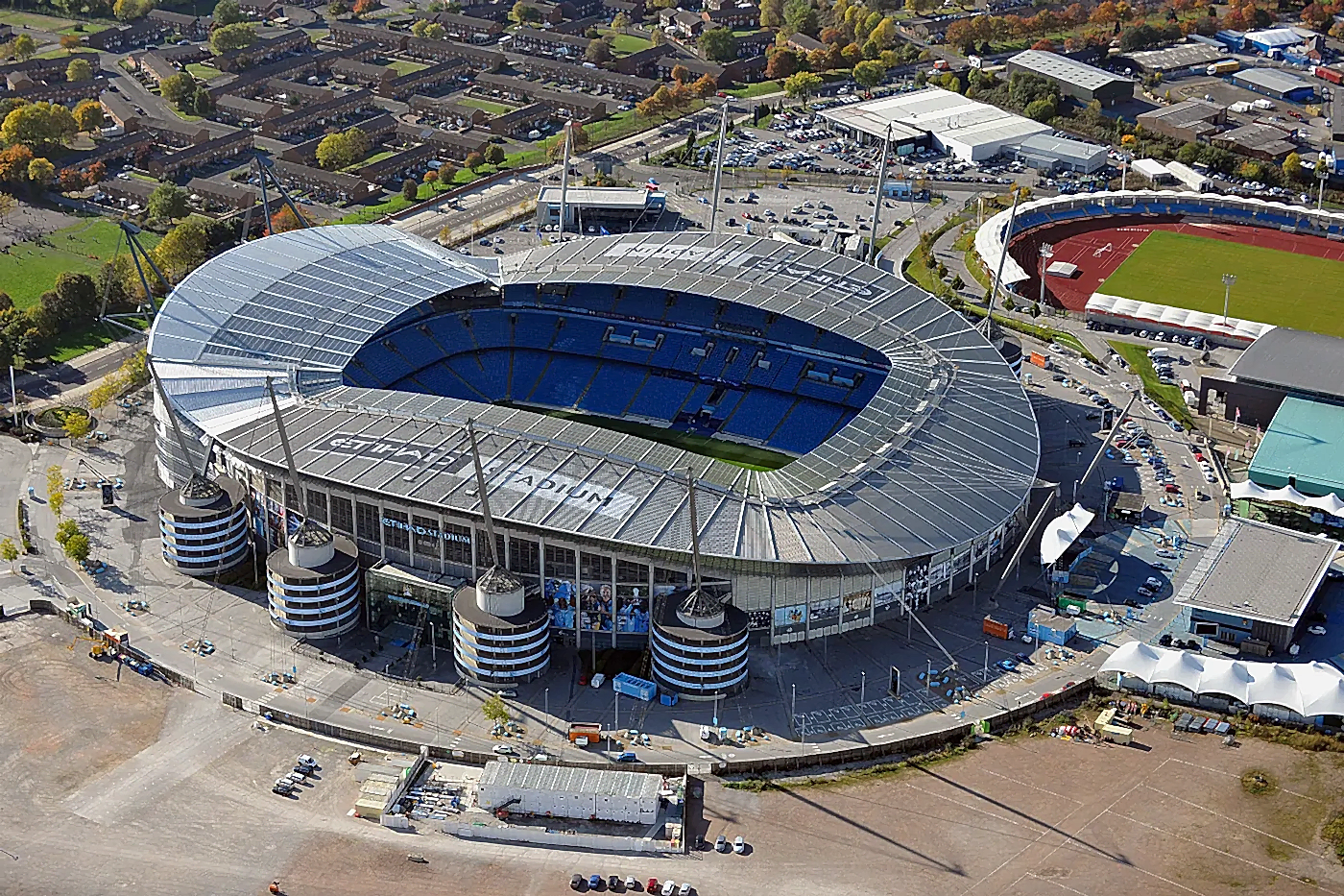 Aerial view of Etihad Stadium in Manchester, showcasing the stadium's structure, surrounding construction area, and clear blue sky, relevant to National Drilling Services' concrete wall sawing project.