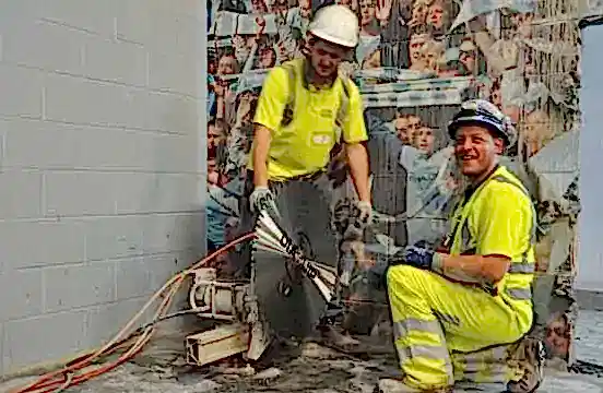 Two workers in safety gear operating a wall saw on reinforced concrete at Etihad Stadium, showcasing precision cutting for refurbishment.