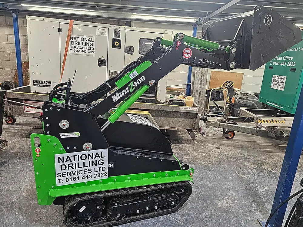 Mini Z 400 electric tracked loader by National Drilling Services, showcasing compact design for confined spaces, with visible branding and operational features in a workshop setting.