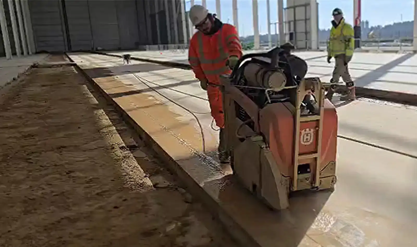 Construction worker operating a concrete cutting machine in a large industrial space, showcasing National Drilling Services' expertise in concrete cutting for construction projects.