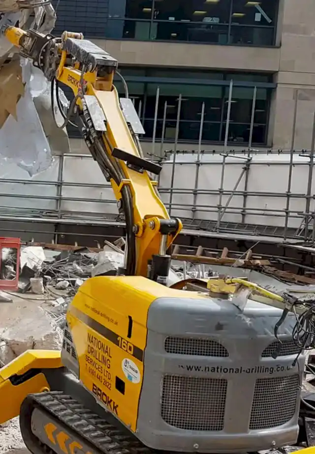 Brokk robotic demolition machine operated by National Drilling Services in construction site, showcasing advanced demolition technology and safety standards.