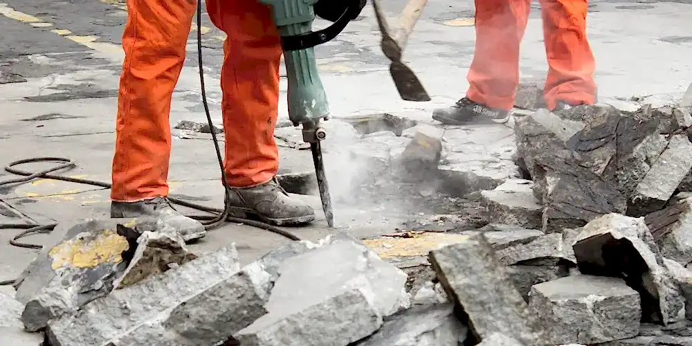 Construction workers using a jackhammer on concrete, with debris scattered around, illustrating precision drilling services for construction and engineering by National Drilling Services.