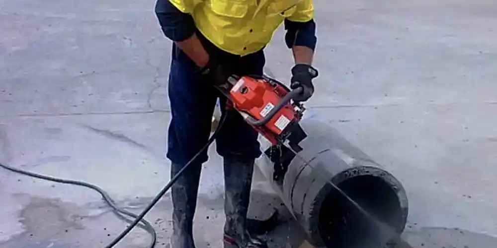 Worker using a concrete chainsaw for precision cutting in construction, demonstrating diamond core drilling capabilities.