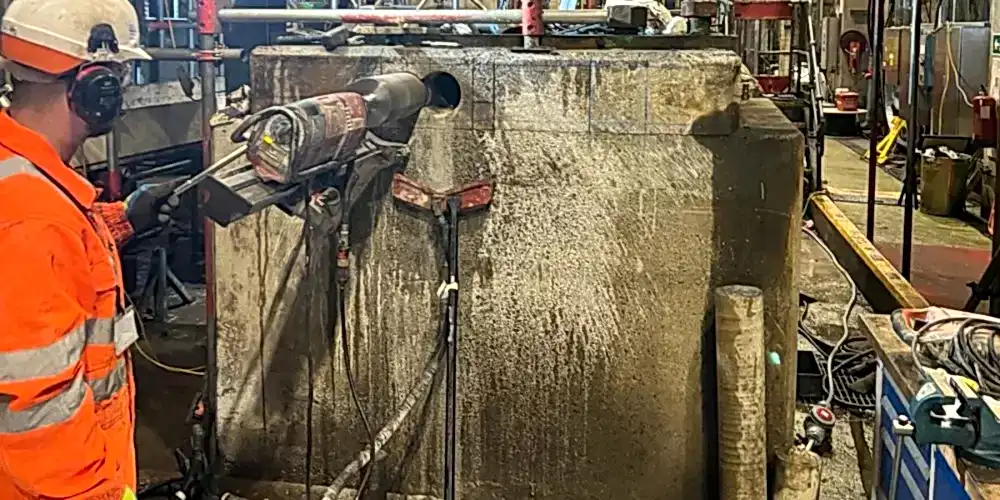Worker operating diamond core drilling equipment on concrete structure in industrial setting, showcasing concrete crunching process for efficient demolition services.