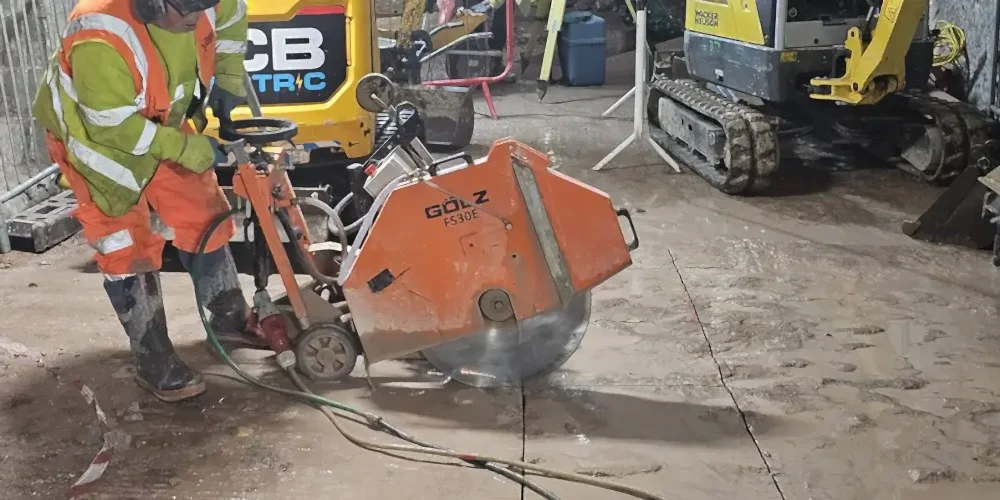 Worker operating a Gölz FS30E electric floor saw on a construction site, showcasing precision cutting capabilities for various materials, relevant to diamond core drilling services.