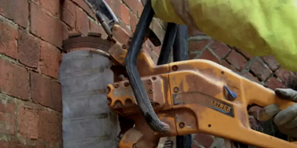 Diamond core drilling tool cutting through brick wall, showcasing precision drilling services by National Drilling Services.